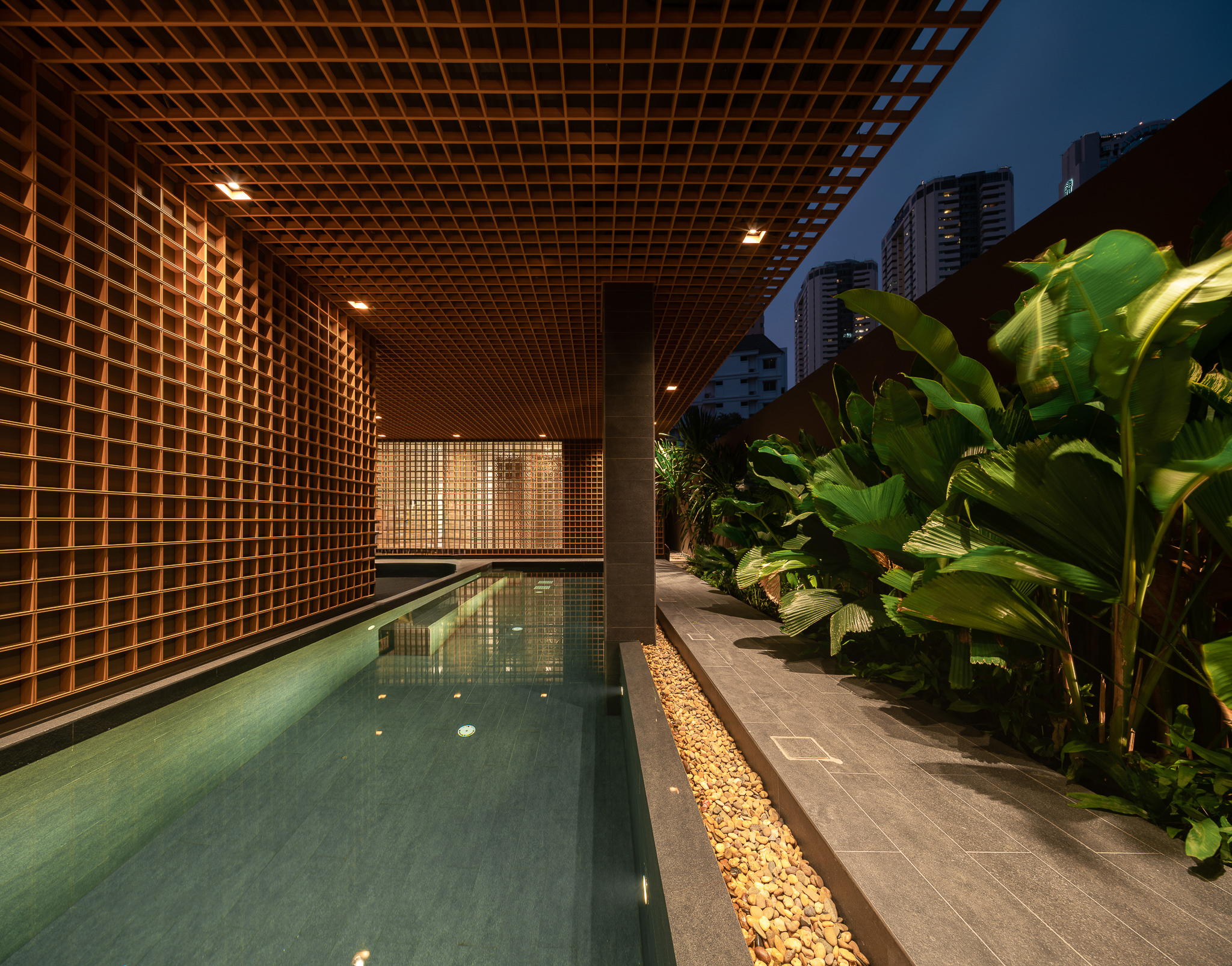 Rooftop lattice-framed pool at night with Bangkok skyline
